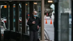 Elderly man wearing mask walking on city street near bus stop