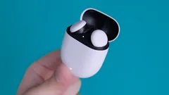 Hand holding white wireless earbuds case with earbuds inside