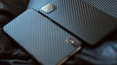 Two black smartphones with textured carbon fiber cases on dark surface