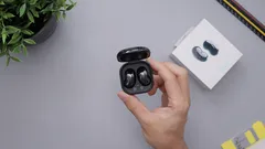 Hand holding black wireless earbuds with charging case on gray surface