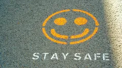 Orange smiley face and white text Stay Safe painted on gray pavement