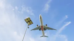 Airplane flying low over streetlight against blue sky with clouds