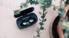 Black wireless earbuds in open charging case on light surface with green plant